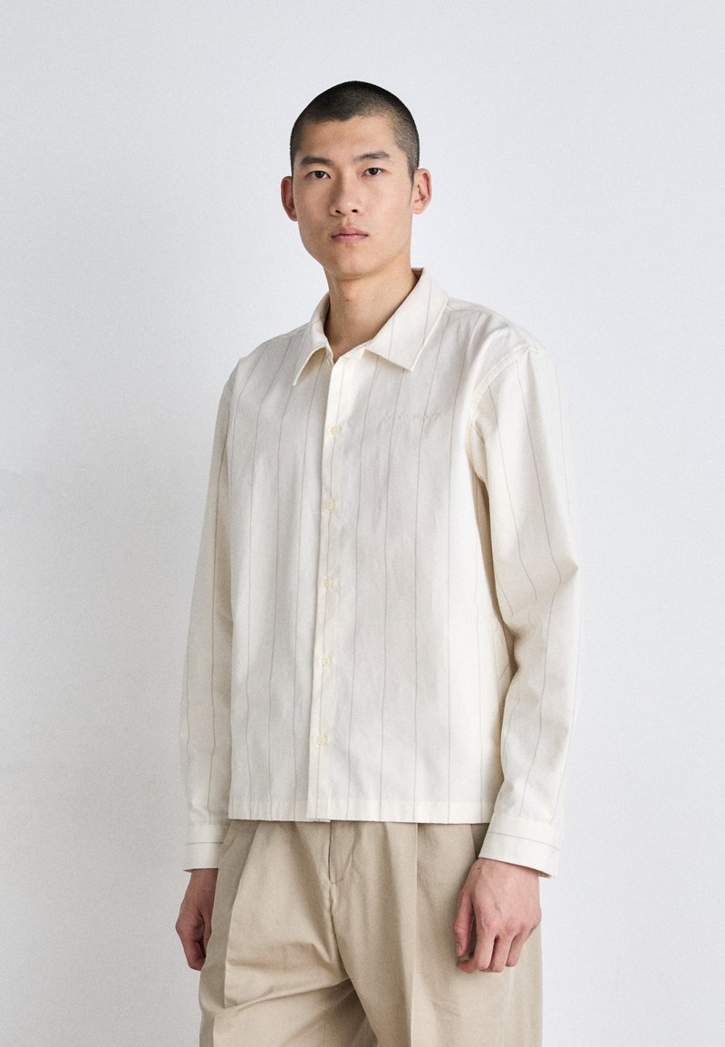 Camicia a maniche lunghe di colore crema con strisce verticali, realizzata in tessuto leggero, dotata di colletto classico e texture morbida.