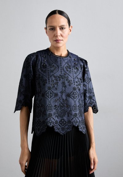 Top brodat de culoare bleumarin, cu motive florale, tiv desfăcut și mâneci până la trei sferturi, având butoane decorativ pe umeri.