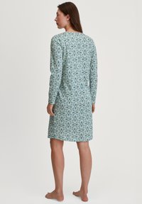 Abito a maniche lunghe realizzato in tessuto morbido, caratterizzato da un motivo floreale blu-verde. Il design è dritto e termina sopra il ginocchio.