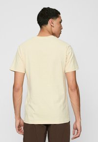 Light yellow cotton t-shirt with short sleeves and a crew neck. Smooth texture, casual fit, and no visible logos or patterns.