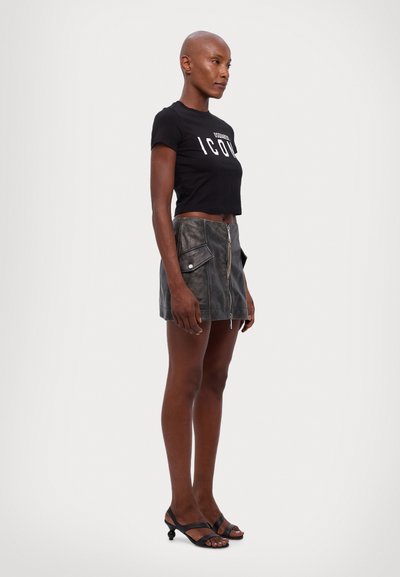Black cropped t-shirt with "ICON" text, paired with a gray leather mini skirt featuring a front zipper and side pockets. Black strappy heels.