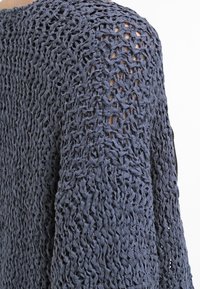 Stickad tröja i mörkblått med öppen vävstruktur, som har en lös passform och långa ärmar. Materialet verkar lätt och luftigt.