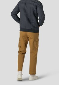 Quiltad mörk jacka med ribbade ärmar, parat med beige cargobyxor med sidofickor, kompletterat med vita sneakers och ankelhöga strumpor.