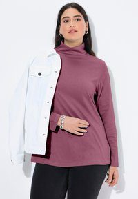 Langärmeliger Rollkragenpullover aus bordeauxrotem Stoff, kombiniert mit einer weißen Denim-Jacke. Das Armband besteht aus runden silbernen Gliedern. Schlichte schwarze Hose.