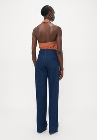 Mørkeblå vidde jeans med høy midje, glidelås og to baklommer. Brukt med en oransje halterneck topp. Glatt denimtekstur.