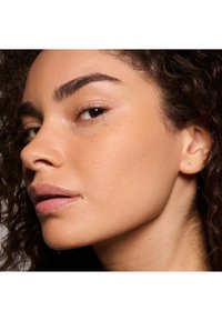 Perfil de un rostro con cabello rizado, tono de piel oliva, pómulos definidos, labios suaves y maquillaje natural, destacando una textura de piel clara.