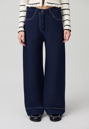Pantaloni a gamba larga color navy con cuciture bianche a contrasto, tasche frontali e chiusura con bottone. Tessuto morbido e vestibilità ampia.
