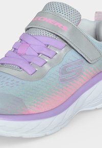 Gros plan sur une basket Skechers colorée avec des lacets lavande, une bride argentée et une tige dégradée pastel réfléchissante.