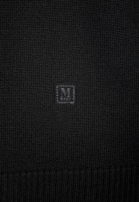 Schwarzer Strickpullover mit geripptem Saum und einem rechteckigen Lederetikett, das das "M"-Logo zeigt. Die Textur ist glatt mit einem gleichmäßigen Muster.