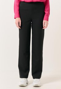 Zwarte, hoge taille broek met een rechtvallend ontwerp. Effen stof zonder opvallende patronen. Gepaarde met witte sportschoenen.
