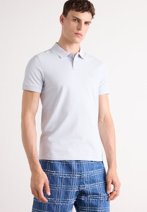 Light blue polo shirt made of soft fabric, featuring a collar, short sleeves, and a small logo patch on the chest. Paired with textured blue shorts.