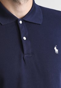 Navy blue polo shirt with two white buttons and a white embroidered horse and polo player logo on the left chest.