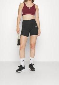 Svarta höga shorts och en maroon sport-bh med vita Adidas-stripes, tillsammans med svarta sneakers och vita Adidas-strumpor.