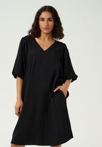 Black short-sleeve dress featuring a V-neck, loose fit, and side pockets, made of a textured fabric with a matte finish.