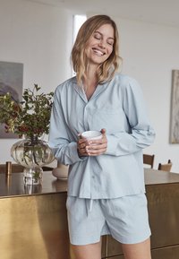 Conjunto de pijama de color azul claro que incluye una camisa de botones con un acabado texturizado y pantalones cortos a juego. La camisa tiene mangas largas y un bolsillo en el pecho.