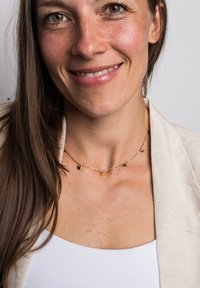 Kuldse ketigaelne kaelakee väikeste ümmarguste ripatsitega. Mudel kannab kreemivärvi jakki valge pluusi peal. Nahatoonus on hele.