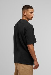 Camiseta de algodón negra con un corte relajado, mangas cortas y cuello redondo. La tela parece suave y tiene una superficie ligeramente texturada.