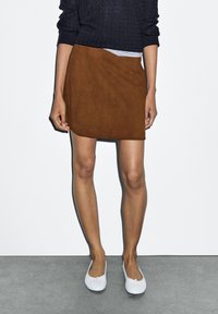 Bruine suède mini-rok met een licht asymmetrische zoom, gecombineerd met lichtkleurige ballerina's en een donkere trui. Glad textuur, eenvoudig ontwerp.