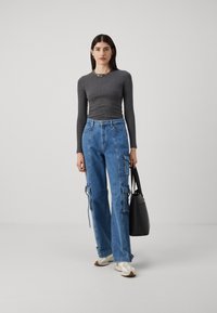 Maglietta grigia a maniche lunghe, jeans cargo blu con tasche laterali e lacci regolabili, sneakers bianche e borsa a tracolla nera. Design semplice e funzionale.