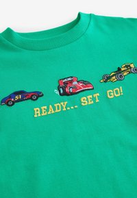 Grön tröja med färgglada broderade racingbilar och texten "Klar... Fart!" i gult. Mjuk textur med ribbat krage.