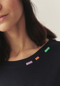 Tumesinine puuvillane topp ümarate kaelustega, millel on värvikad tikandaccentid rohelistes, oranžides ja lilla toonides kaeluse lähedal.