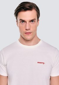 Balta medvilninė marškinėliai trumpomis rankovėmis ir raukšlėta apykakle. Pasižymi raudonu tekstu "merry.", kuris yra kairėje krūtinės pusėje.