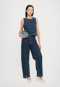 Denim mouwloos topje met rafelzoom, gecombineerd met hoge taille, wijdvallende denimbroek. Geaccessoriseerd met een blauwe textuur clutch; witte hakken.