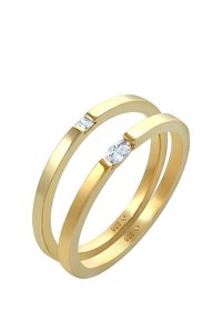 To interlockede guld ringe, hvoraf den ene har en marquise-formet diamantaccent. Glat tekstur, enkelt design, med synlige mærkninger for metalrenhed.