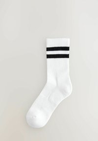 Bílá bavlněná ponožka s žebrovanou texturou, vybavená dvěma černými vodorovnými pruhy blízko vrchu. Hladký design špičky a kotníku.