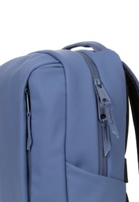 Sac à dos bleu, au texture douce, au design élégant avec des zips, une poignée supérieure et une poche latérale pour un accès facile.