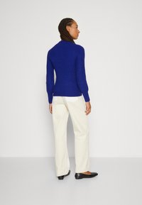 Blue knitted sweater with long sleeves and a fitted design, paired with cream wide-leg trousers and black flats, viewed from the back.
