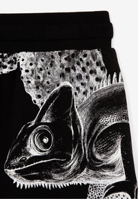 Tela negra con una ilustración blanca detallada de un camaleón, que resalta su piel texturada y sus ojos prominentes.