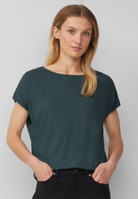 Haut court à manches courtes de couleur vert foncé avec un col rond, texture lisse, coupe décontractée et manches retroussées, associé à un pantalon noir.