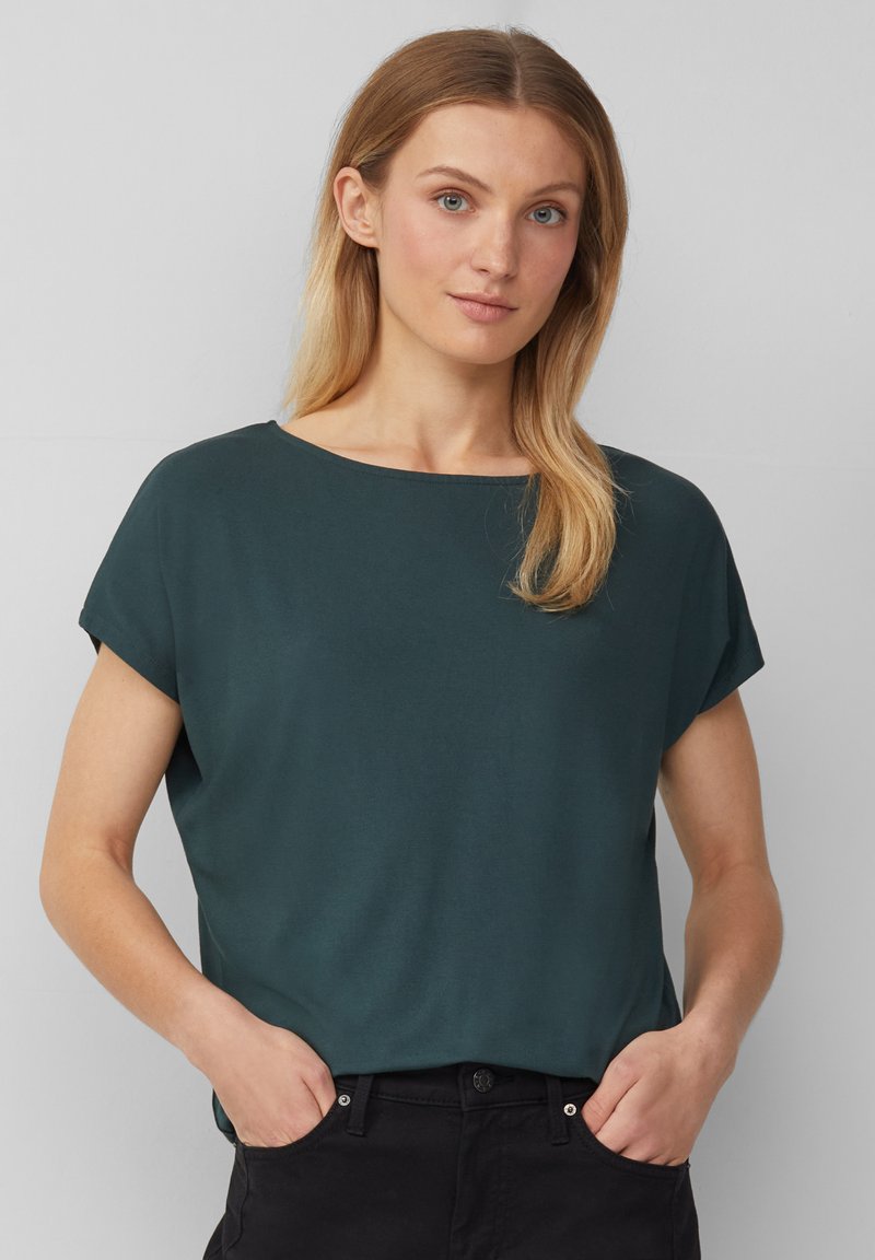 Haut court à manches courtes de couleur vert foncé avec un col rond, texture lisse, coupe décontractée et manches retroussées, associé à un pantalon noir.