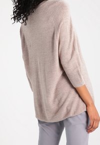 Pull en maille beige clair avec manches trois-quarts et coupe décontractée. Texture côtelée et rayures horizontales subtiles qui mettent en valeur le design.