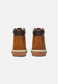 Stivali alla caviglia in suede marrone con colletto in pelle scura, suola intermedia bianca e suola in gomma. Presentano cuciture a contrasto e un design robusto.