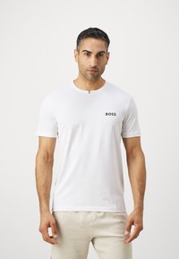 Valge lühikeste varrukatega T-särk, mis on valmistatud siledast kangast, ringja kaelusega ja väikese musta "BOSS" logoga rinnal.