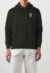 Felpa nera con cappuccio realizzata in tessuto morbido, con tasca frontale e un design in bianco a fumetti sul petto. Maniche lunghe con dettagli testuali.