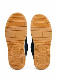 Suole delle scarpe con un design in gomma testurizzata, di colore marrone-arancio. Stampate con il marchio "TOMMY JEANS" sulla superficie.