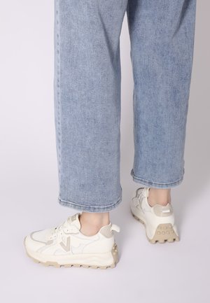 Witte sportschoenen met beige accenten, gemaakt van mesh en synthetische materialen, met een gestructureerde zool en een lus aan de hak. Draagt bij lichte blauwe spijkerbroek.