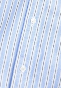 Tissu rayé bleu et blanc avec des lignes verticales et deux boutons blancs cousus sur la patte de devant d’une chemise.