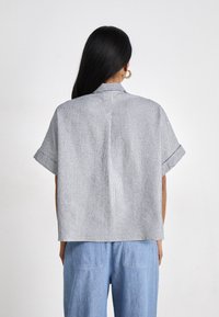 Camicia a maniche corte con colletto in tessuto a righe blu e bianche. Forma ampia con risvolti sulle maniche e piega sul retro per aggiungere texture e movimento.