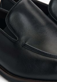 Zwarte leren loafers met een gladde textuur, slip-on ontwerp en subtiele stiksels langs de bovenkant. Rubberen zool voor grip.