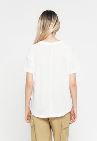 Person with long blonde hair wearing a plain white short-sleeve shirt and beige cargo pants, shown from the back against a white background.