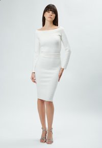 Abito bianco scivolato sulle spalle con maniche lunghe e silhouette a tubino aderente. Tessuto testurizzato con un motivo delicato e vita cintata.