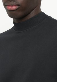 Top nero a collo alto realizzato in tessuto liscio, con un design aderente e un colletto a costine, che mette in mostra una sottile texture e dettagli delle cuciture.