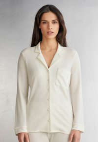 Lichtcrème pyjama-top met ribbelstructuur, voorzien van een kraag, een borstzak en knoopsluiting aan de voorkant. Lange mouwen.