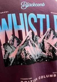 Vinrød bomulds t-shirt med bjerggrafik; har blå og lyserøde tekster "WHISTLER" og "BLACKCOMB" ovenover, med "BRITISH COLUMBIA" nedenunder.