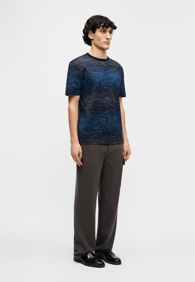 Short-sleeve, crew-neck T-shirt in dark blue, featuring a textured, gradient pattern. Paired with loose-fitting gray trousers and black shoes.