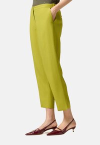 Pantalons cropped en lin vert avec poches latérales, associés à des escarpins à bride arrière en cuir verni bordeaux avec un bout pointu et un petit talon.